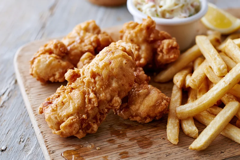 Beer-battered fried fish pieces and golden french fries served on a wooden board with coleslaw and lemon wedge