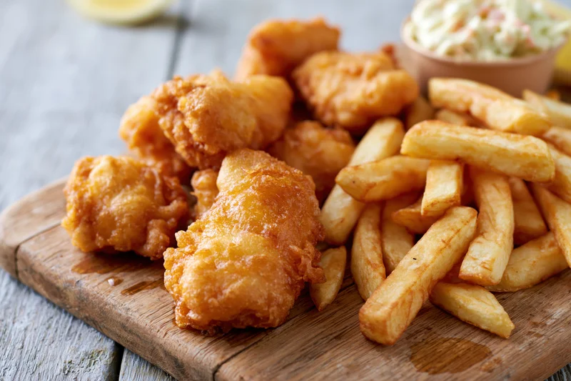 Fried fish and french fries served on a wooden board with tartar sauce