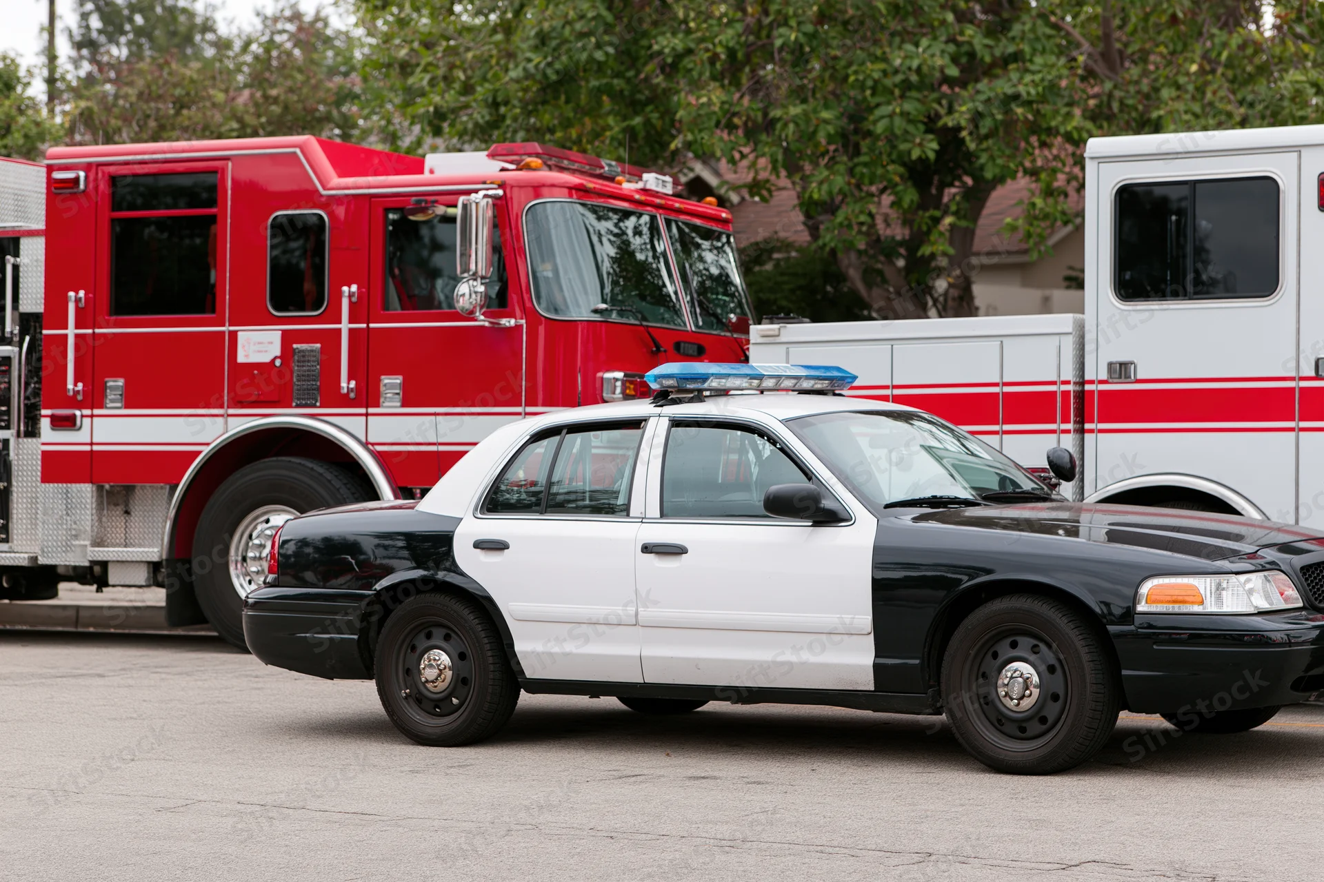 Black and white police cruiser parked in front of red fire truck and white ambulance on asphalt street