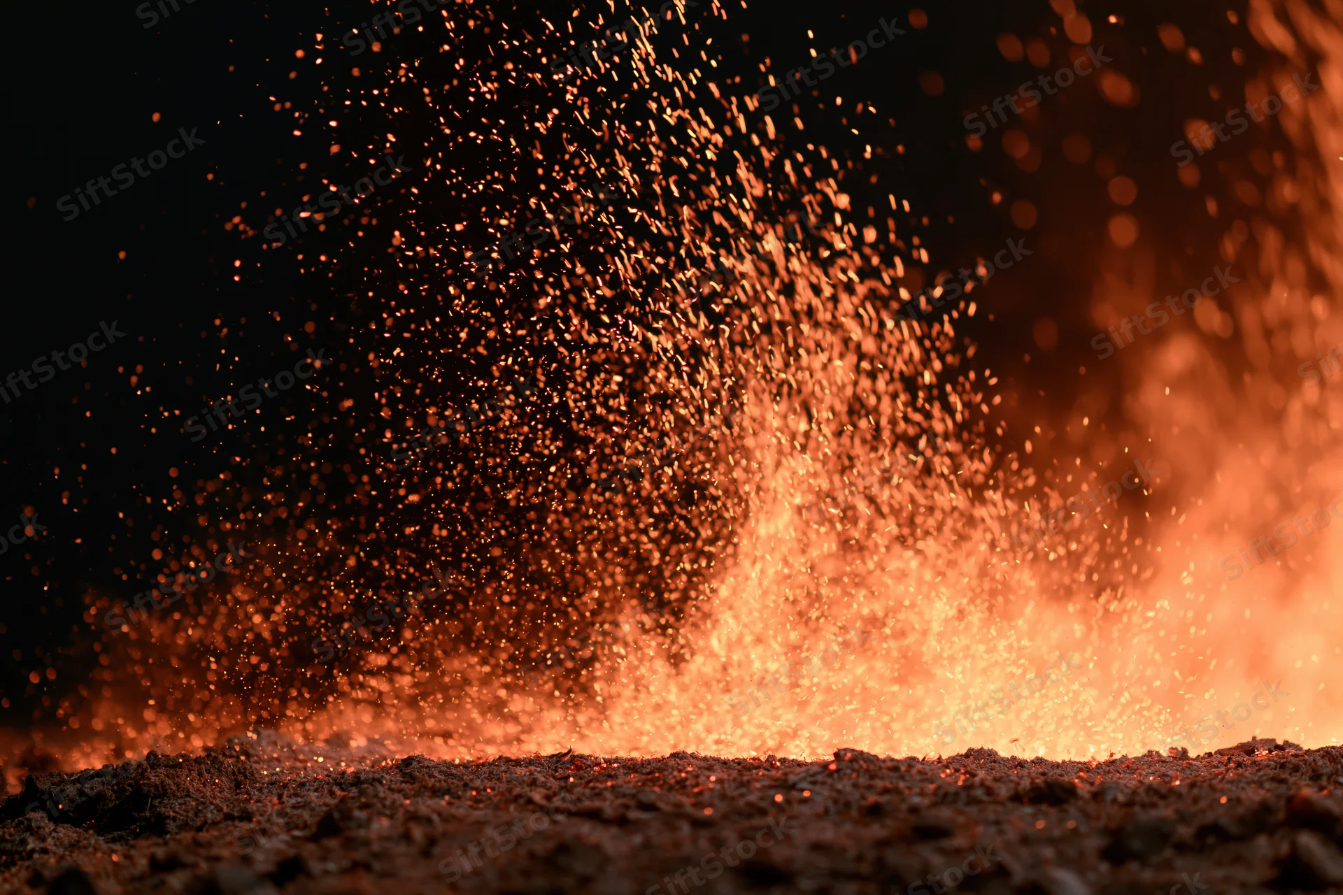 Glowing ember sparks bursting upward from a burning surface at night