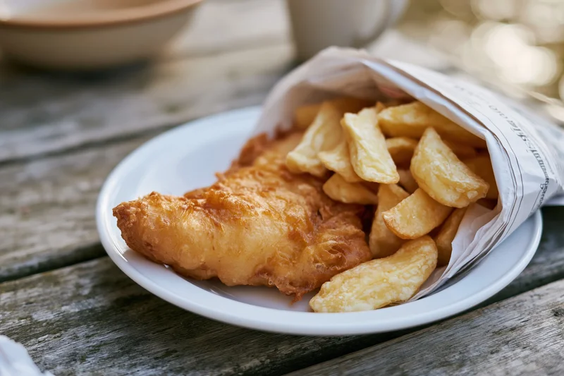 Golden fried fish and chips served on a white ceramic plate on a wooden table