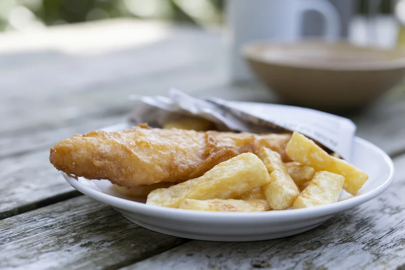 Golden fried fish and chips on a white ceramic plate on a wooden table outdoors