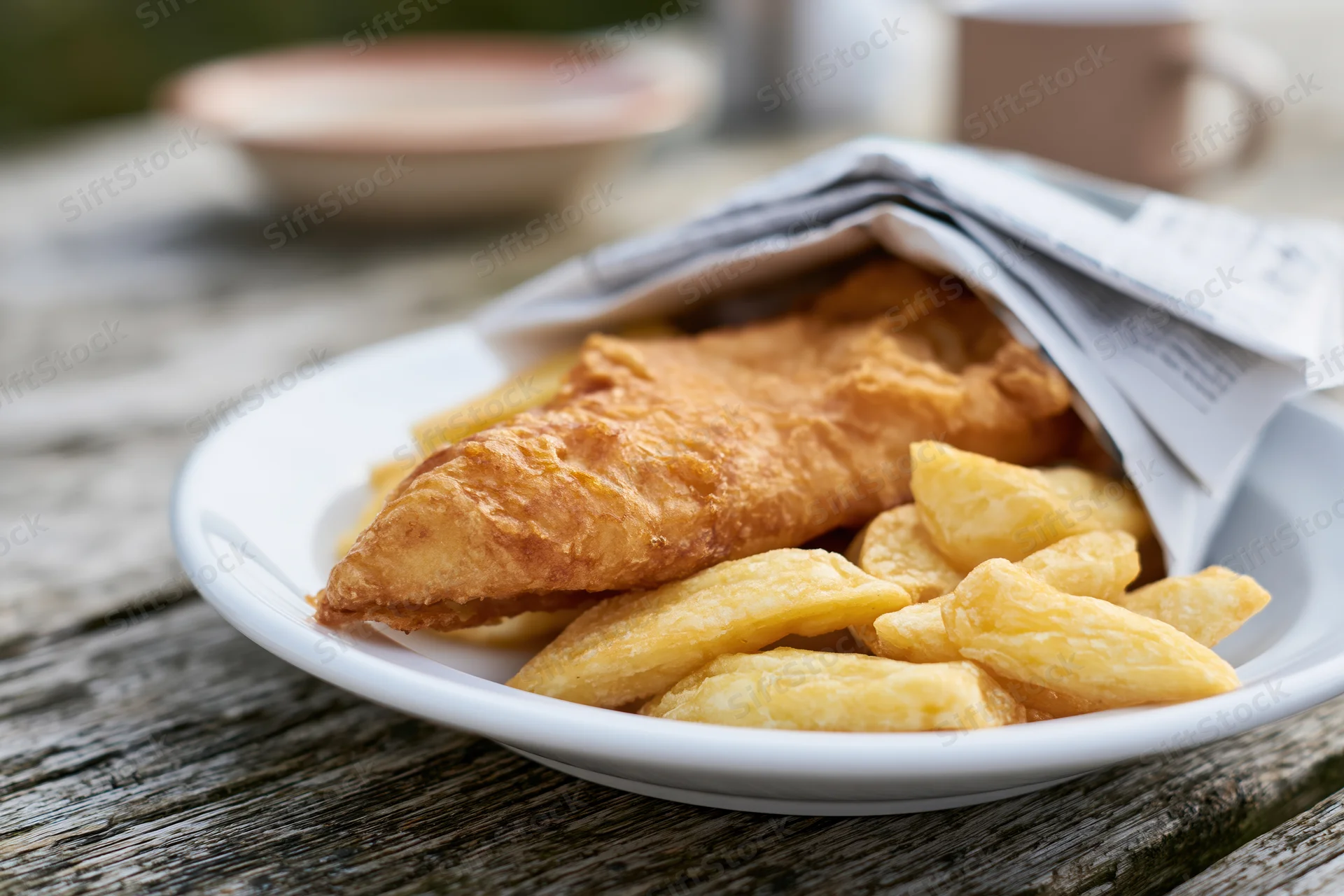 Golden fried fish and chips on a white plate resting on a wooden table