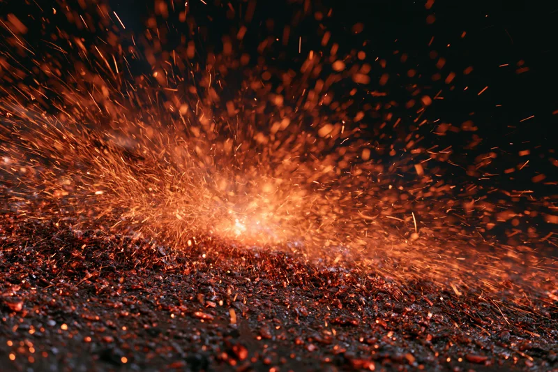 Burst of glowing sparks exploding outward from a central point on a dark textured surface