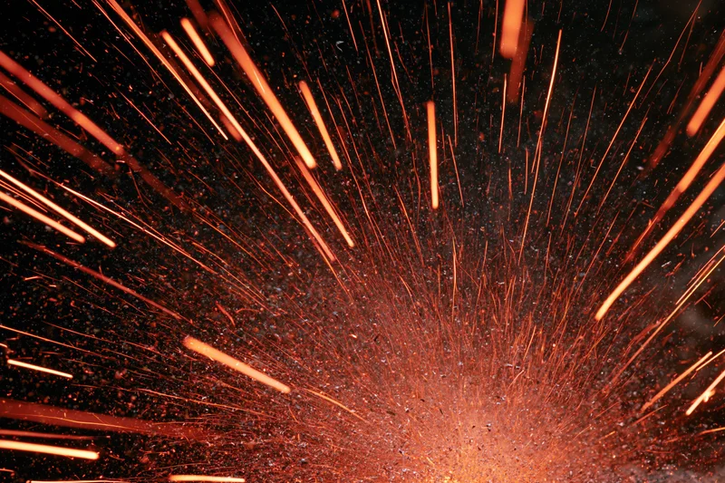 Burst of glowing orange sparks radiating outward from a central point against a dark background
