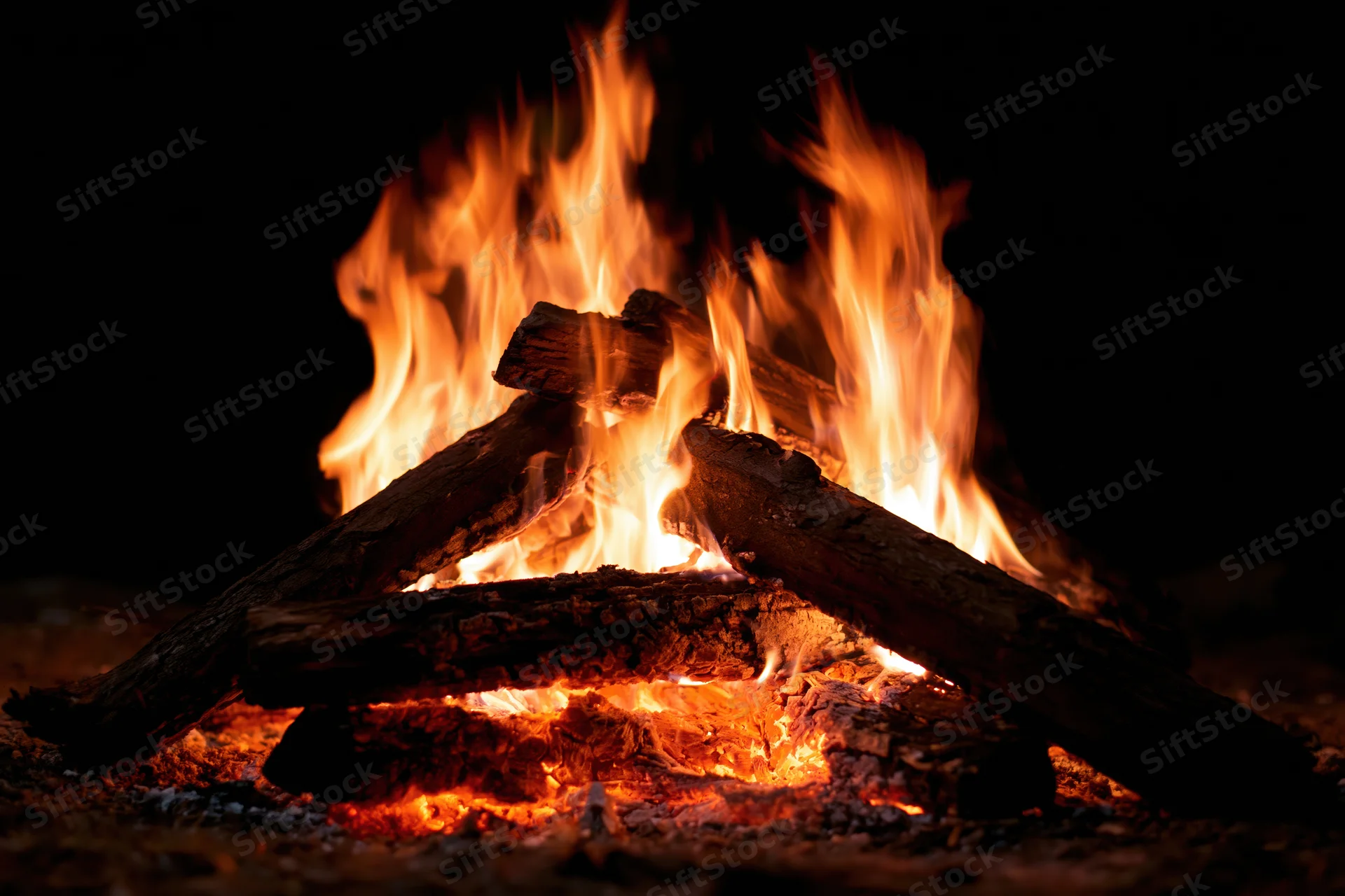 Campfire burning with stacked logs at night outdoors