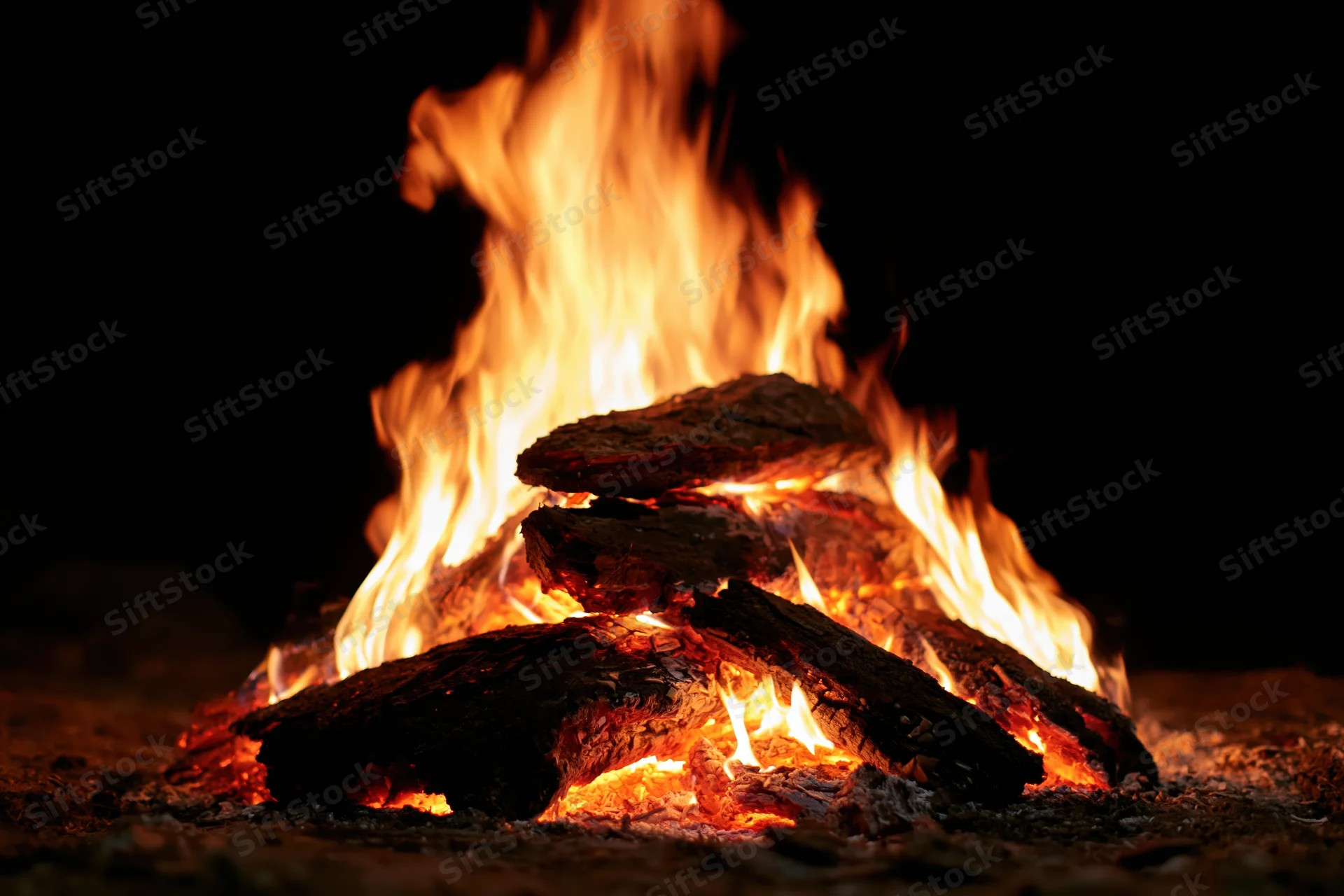 Campfire burning with stacked logs at night outdoors