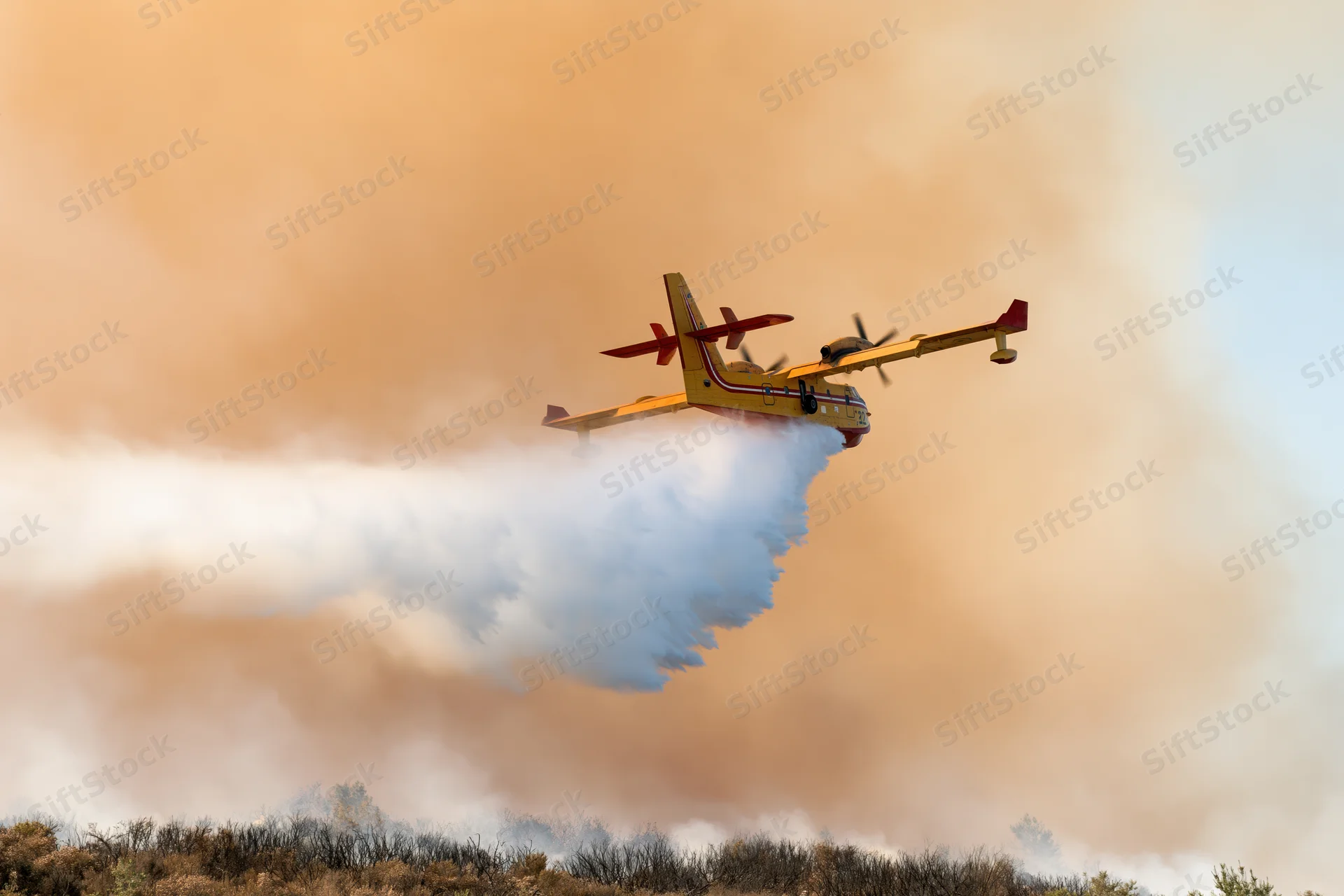 Canadair cl415 firefighting aircraft releasing water over wildfire smoke plume