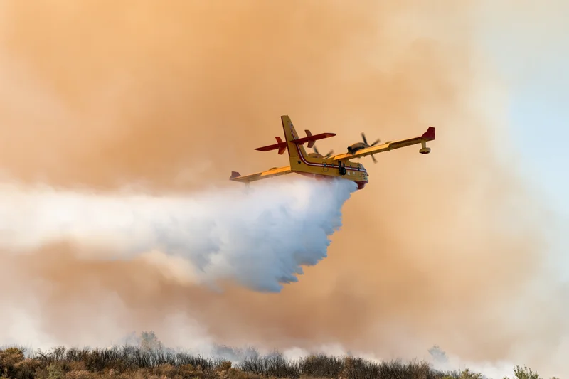 Canadair cl415 firefighting aircraft releasing water over wildfire smoke plume
