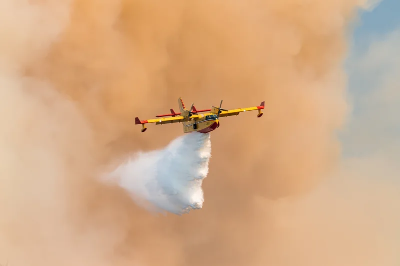 Canadair cl415 firefighting aircraft releasing water over smoke-filled sky