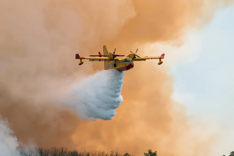 Yellow canadair cl415 aircraft releasing water over wildfire smoke plume in sky