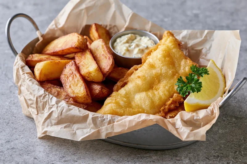 Fish and chips served in a metal basket lined with paper on a gray surface