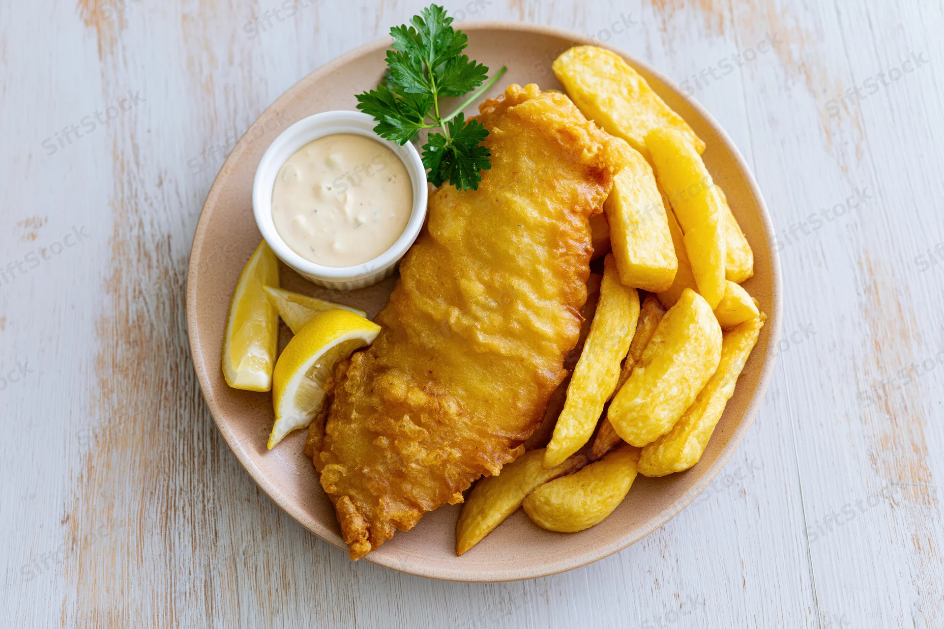 Golden fried fish and chips served on a round beige ceramic plate with lemon wedges and tartar sauce