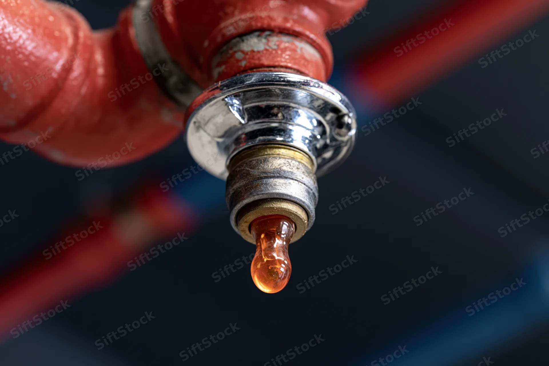 Fire sprinkler head dripping amber liquid from red pipe in close-up view