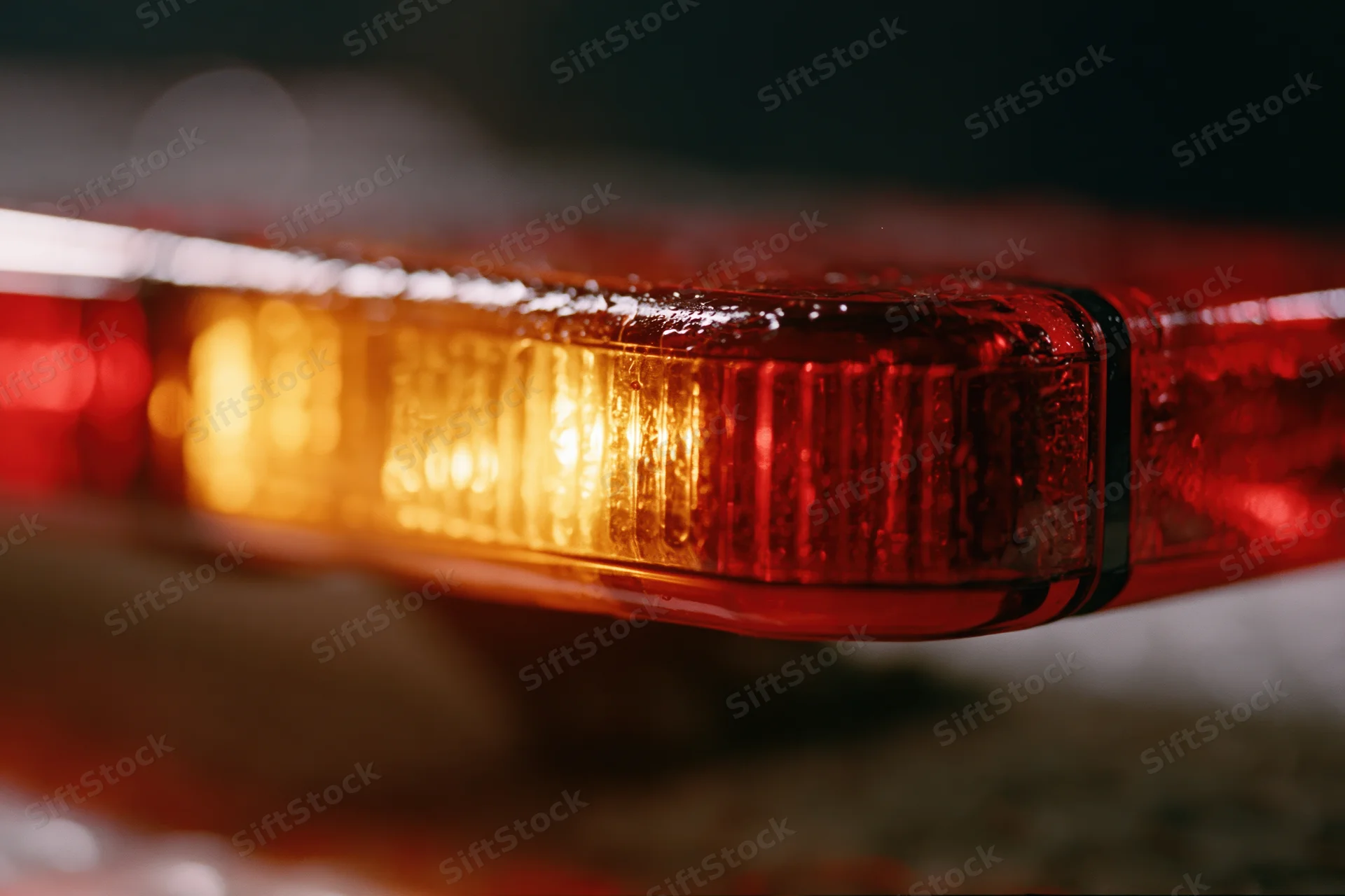Close-up of a flashing red and amber emergency vehicle light bar mounted on top of a vehicle at night in the rain