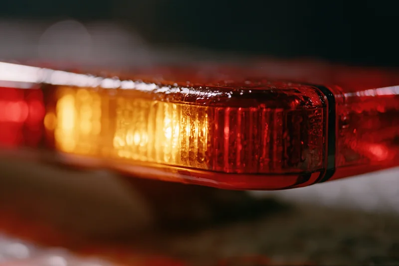 Close-up of a flashing red and amber emergency vehicle light bar mounted on top of a vehicle at night in the rain