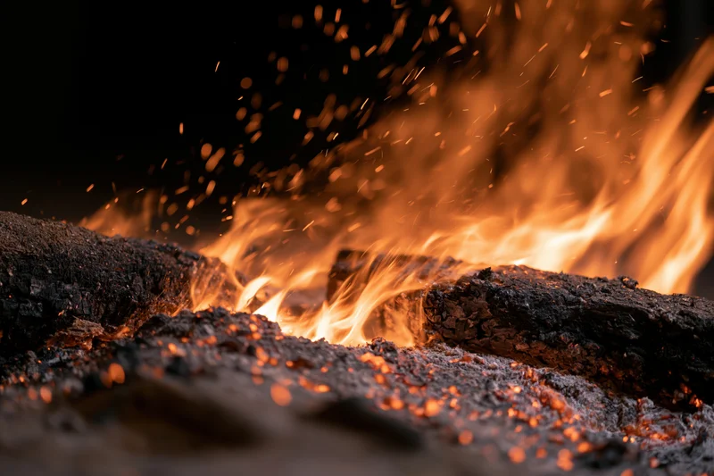 Close-up of burning campfire logs with dancing flames and flying sparks at night