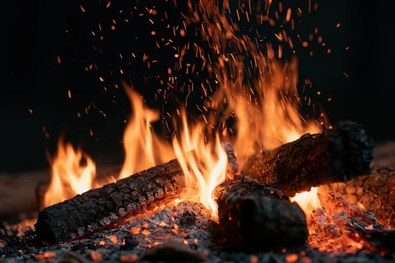 Close-up of burning logs with dancing flames and flying sparks at night