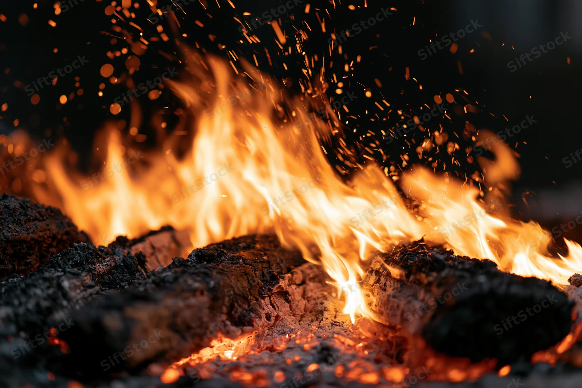 Close-up of burning campfire logs with dancing flames and flying sparks at night
