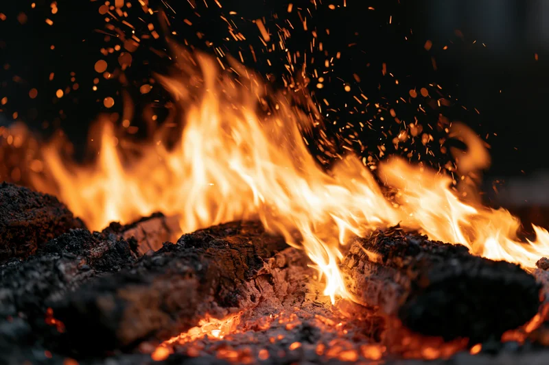 Close-up of burning campfire logs with dancing flames and flying sparks at night