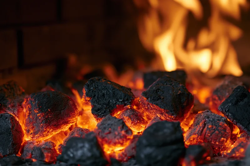 Glowing coal embers burning in a fireplace with flames in the background