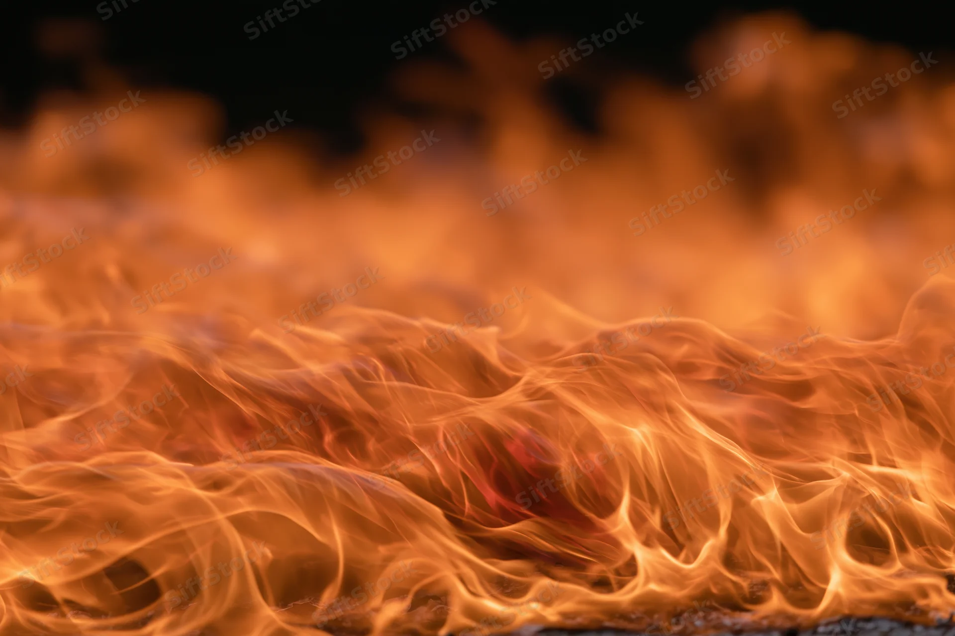 Close-up of intense flames burning across the frame with glowing orange and red tongues against a dark background
