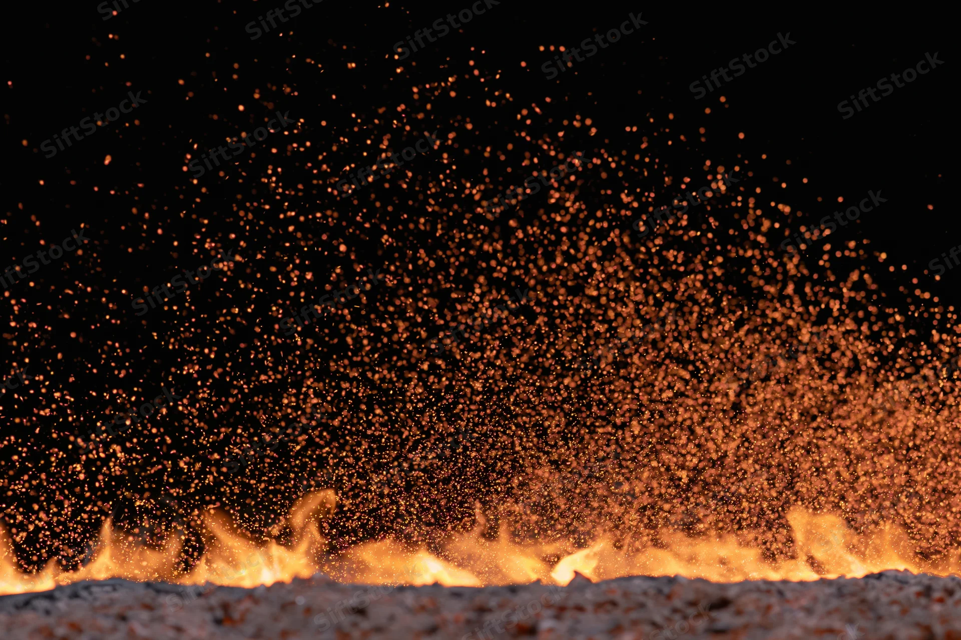 Flames burning along the ground with sparks rising into the dark night