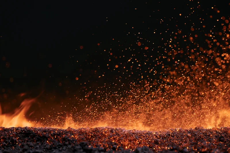 Close-up of fire flames and flying sparks along the bottom of the frame against a dark background