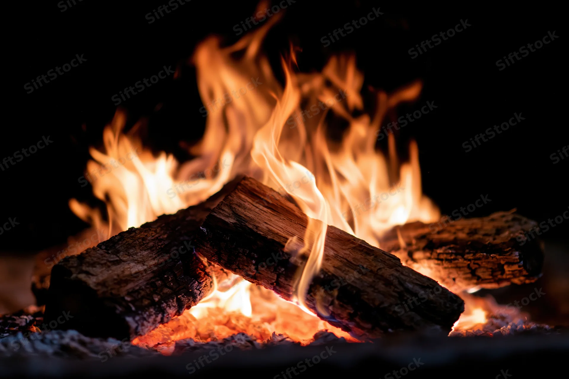 Burning wood logs with bright orange and yellow flames in a dark fireplace setting