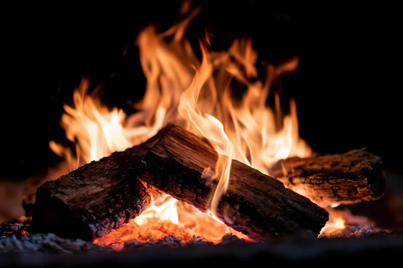 Burning wood logs with bright orange and yellow flames in a dark fireplace setting