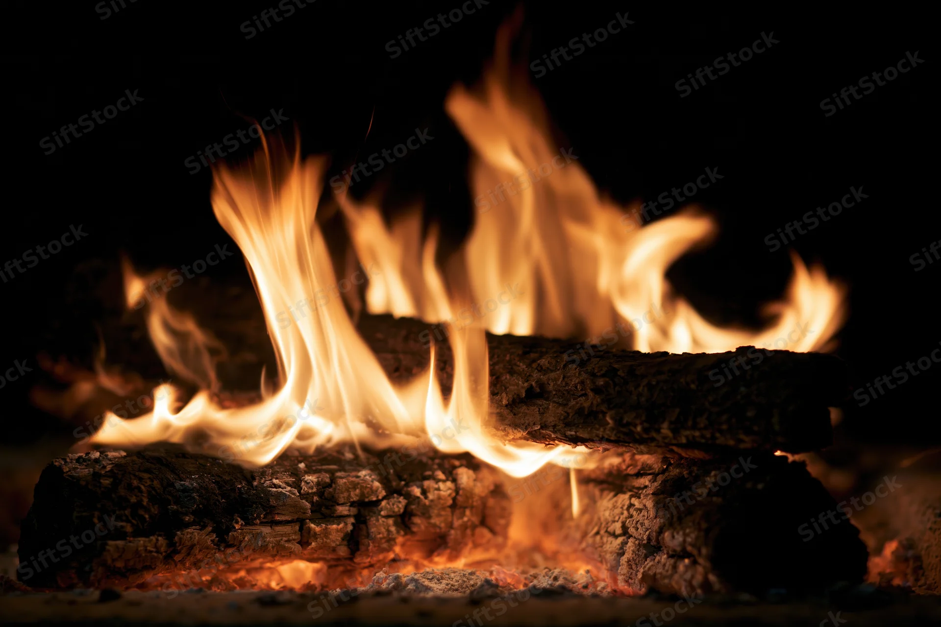 Close-up of burning wood logs with bright orange and yellow flames in a dark setting