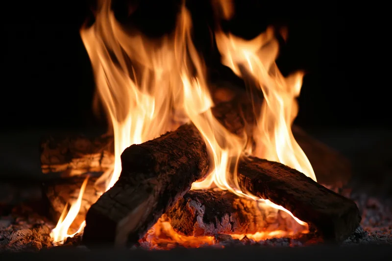 Close-up of burning wood logs with bright orange and yellow flames at night