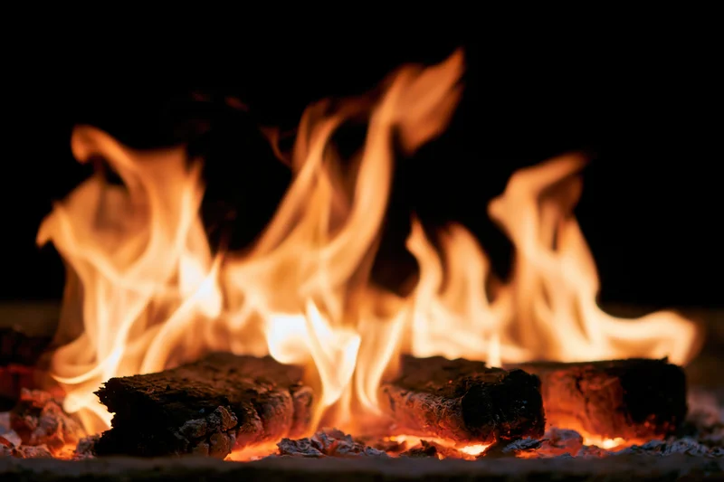 Close-up of burning wood logs with orange and yellow flames in a dark fireplace