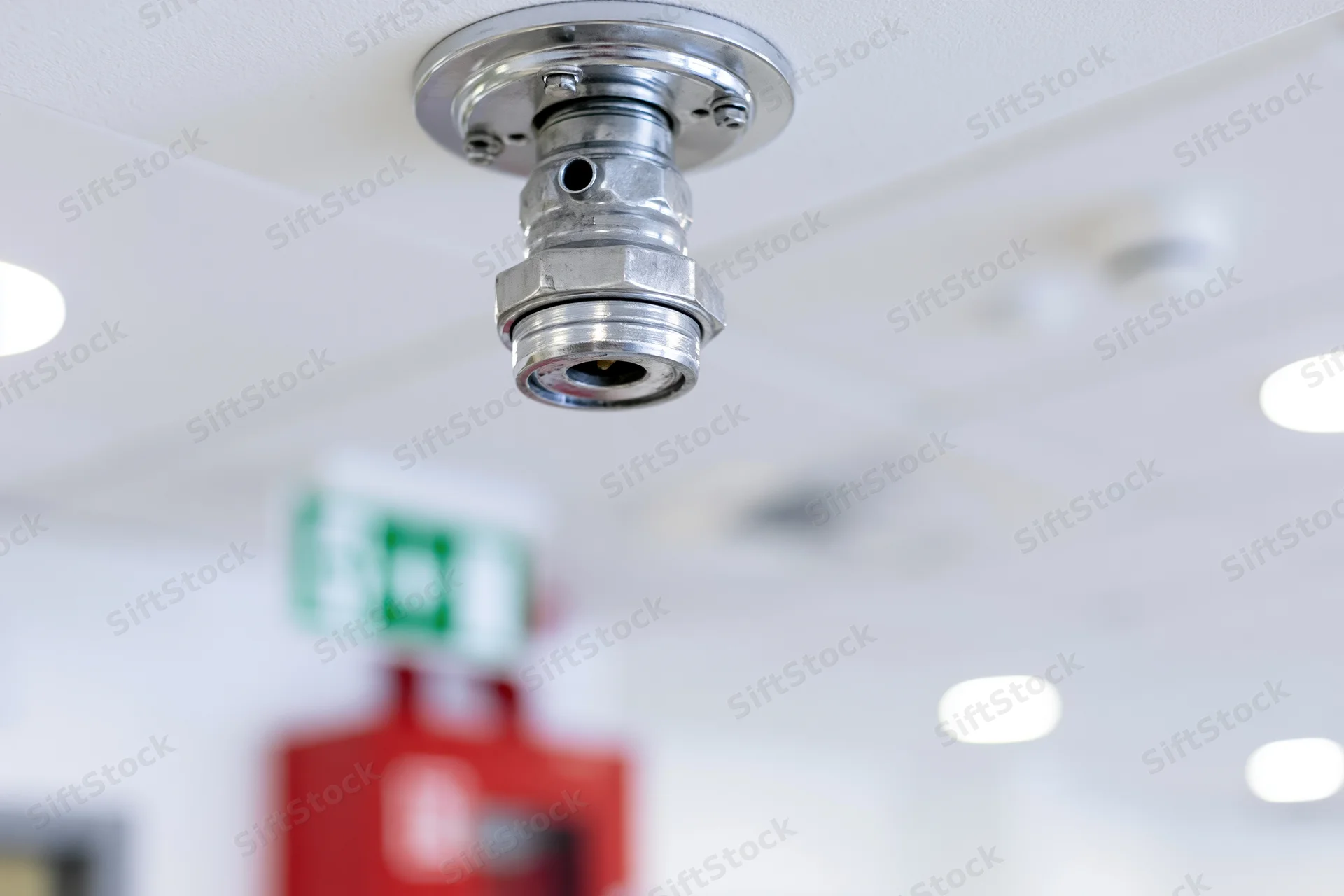 Chrome fire sprinkler head mounted on white ceiling in commercial building interior