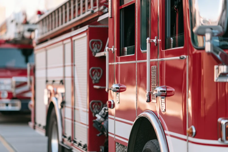 Red firetruck parked outside fire station with chrome details and ladder on side