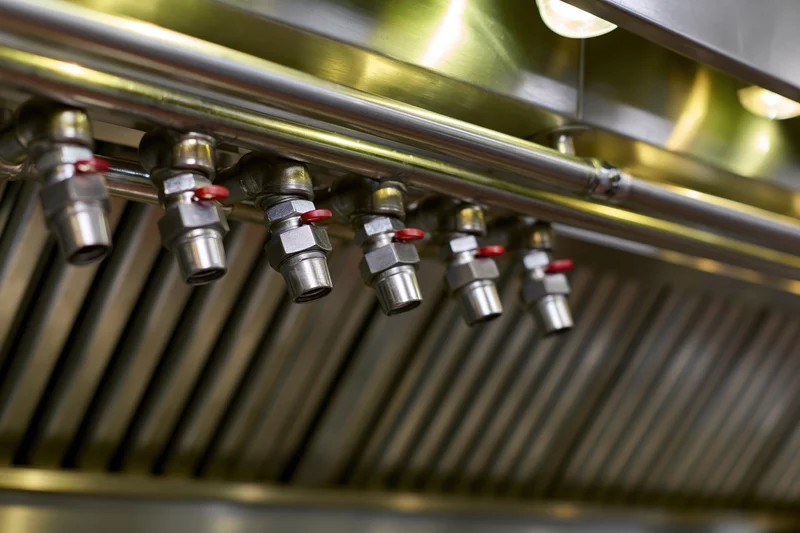 Fire suppression nozzles mounted in a row along the ceiling of a commercial kitchen
