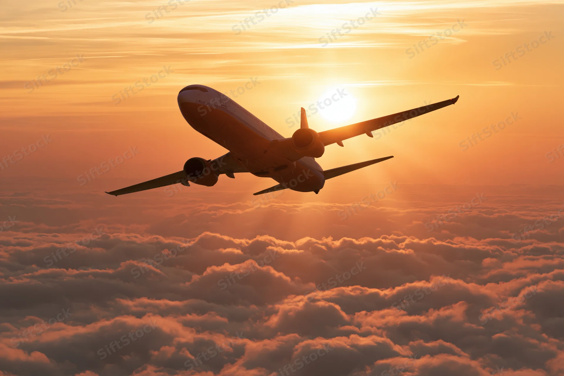 Commercial passenger jet flying above cloud layer at sunset