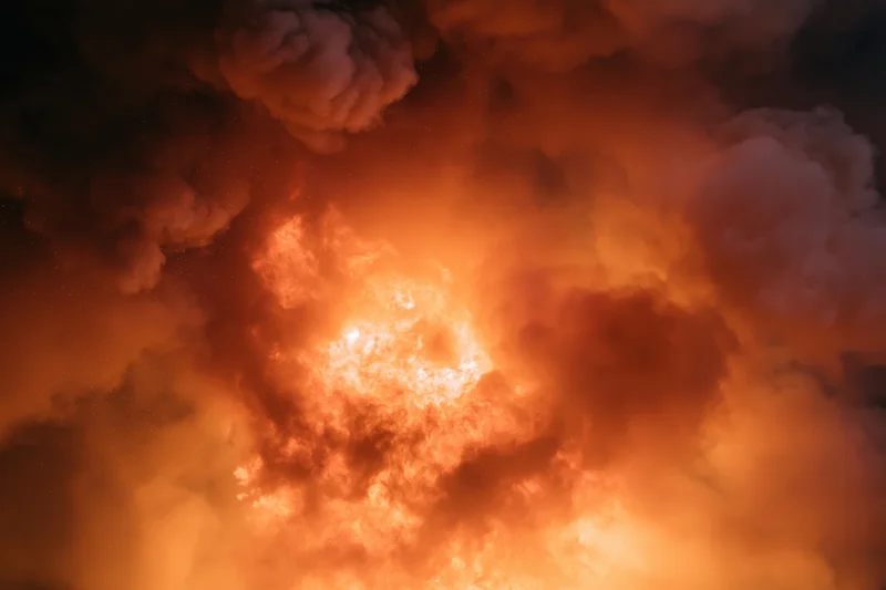 Dense smoke and ember clouds from an industrial fire filling the sky at night