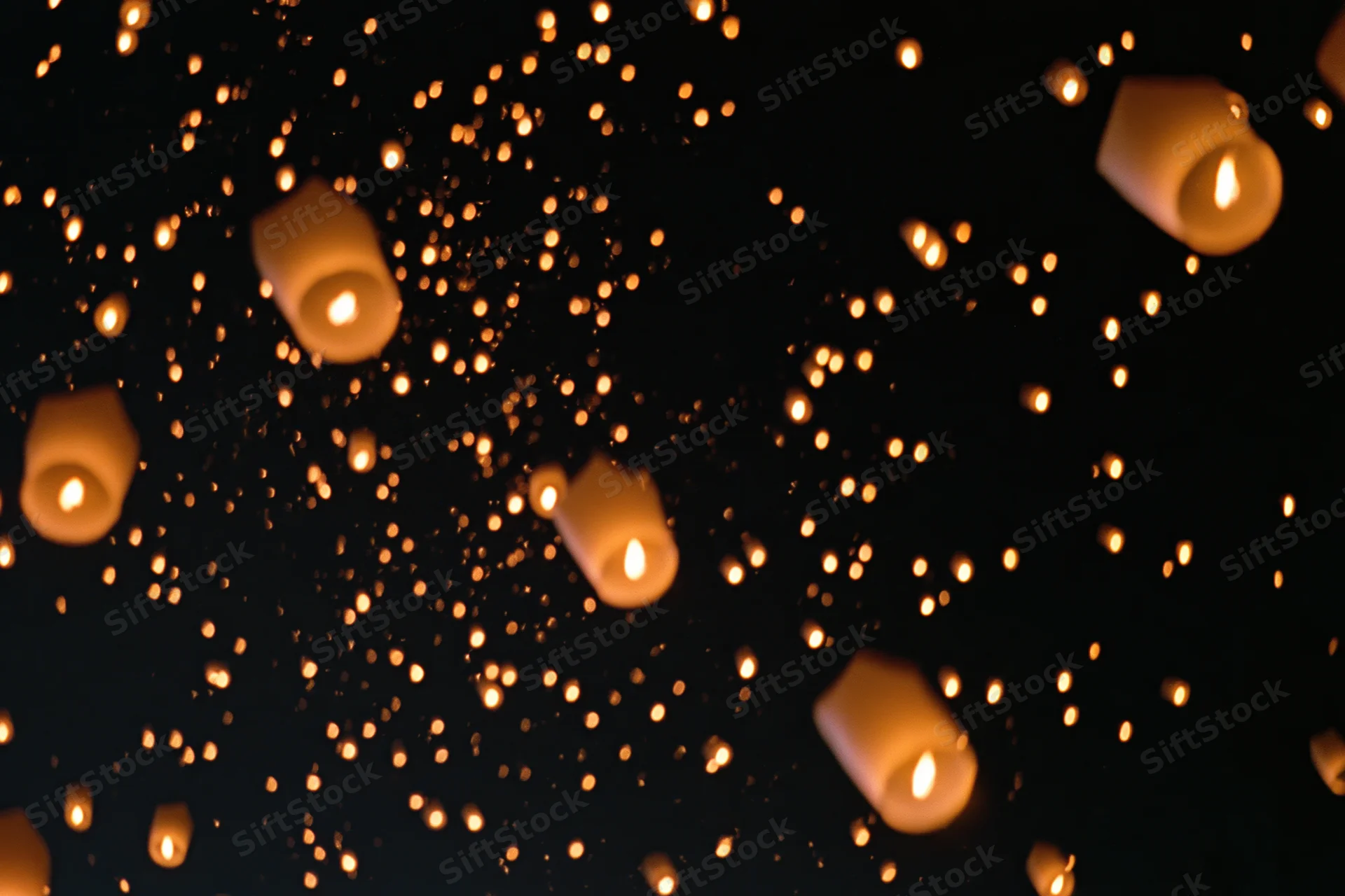Sky lanterns floating upward with glowing embers drifting in the dark night sky