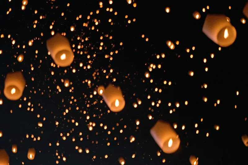 Sky lanterns floating upward with glowing embers drifting in the dark night sky