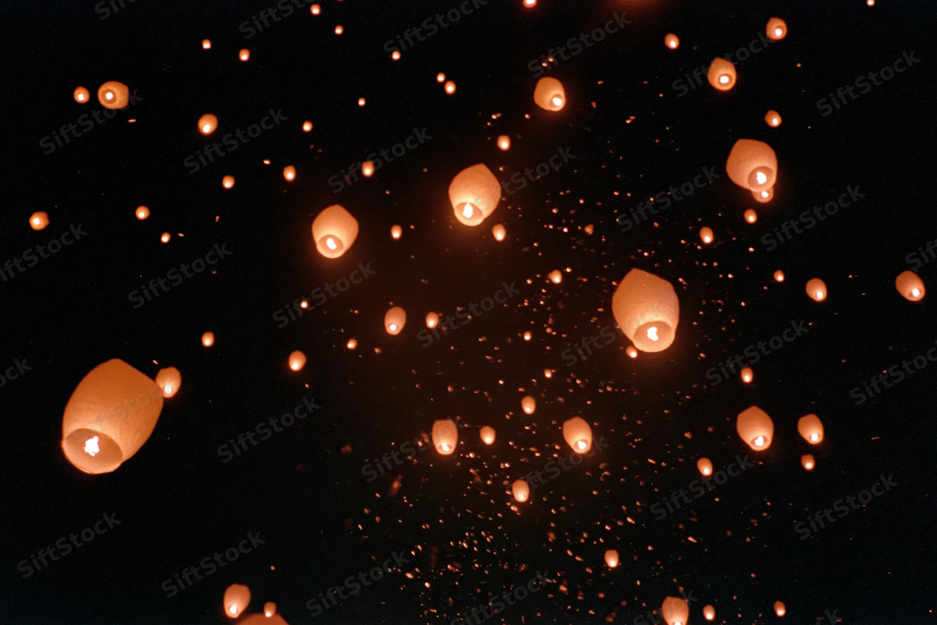 Glowing sky lanterns and ember sparks drifting upward in the night sky