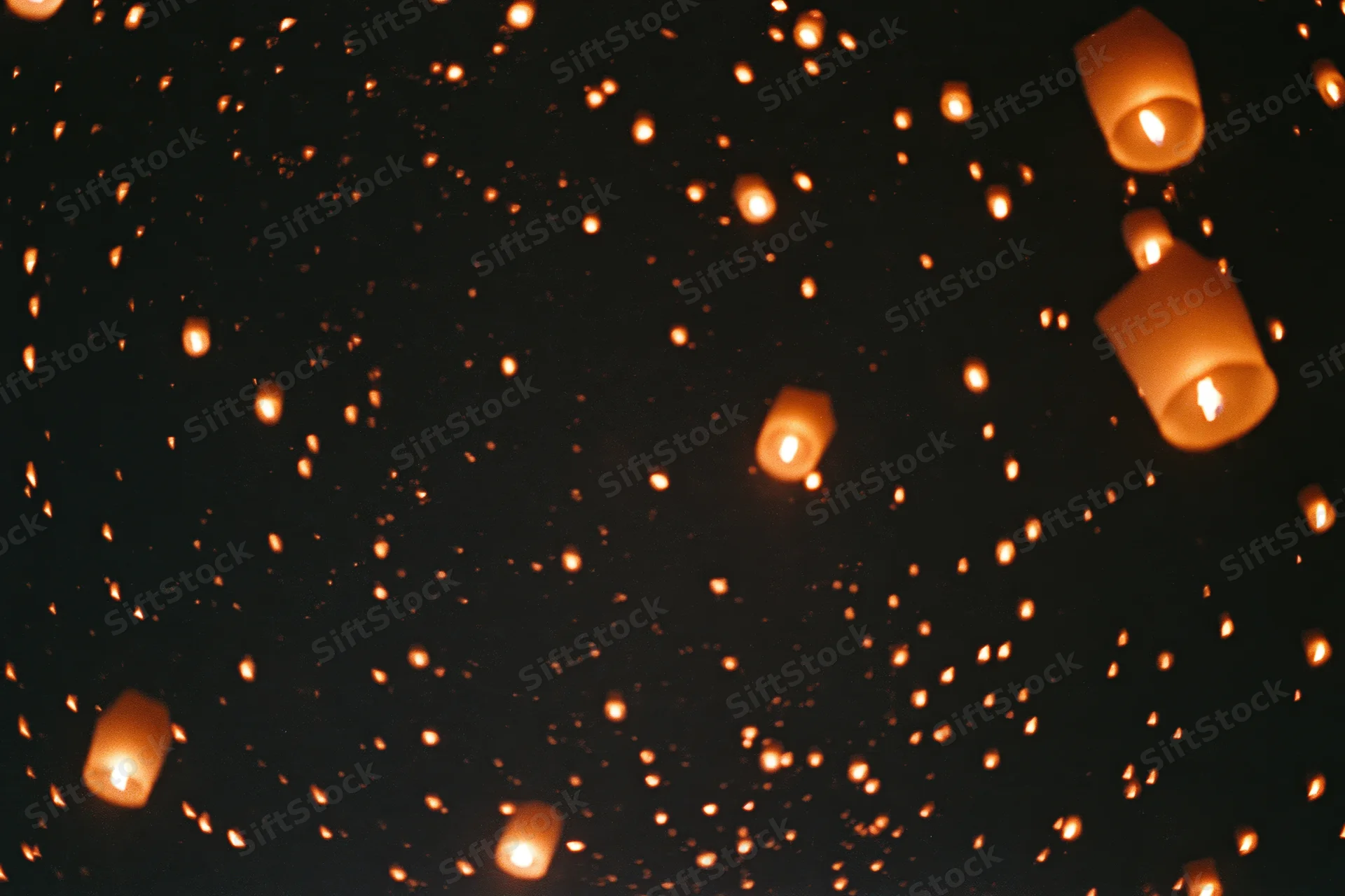 Sky lanterns floating upward in dark night sky with glowing embers drifting around