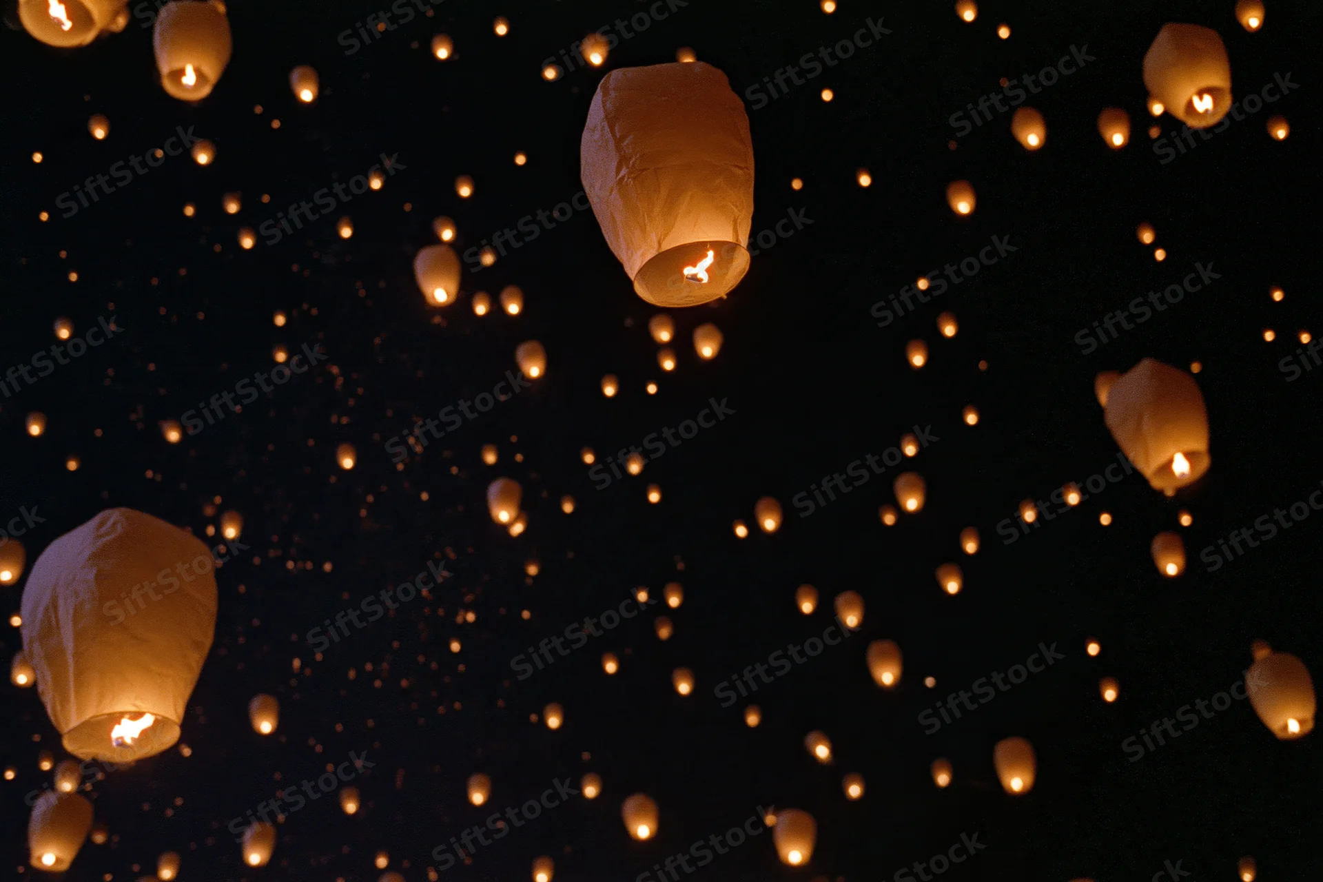 Sky lanterns floating upward in the night sky with glowing embers drifting around them