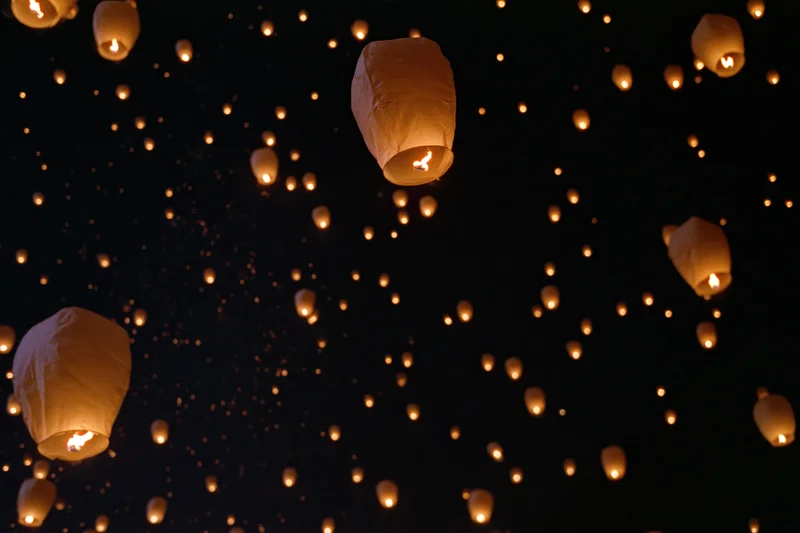 Sky lanterns floating upward in the night sky with glowing embers drifting around them
