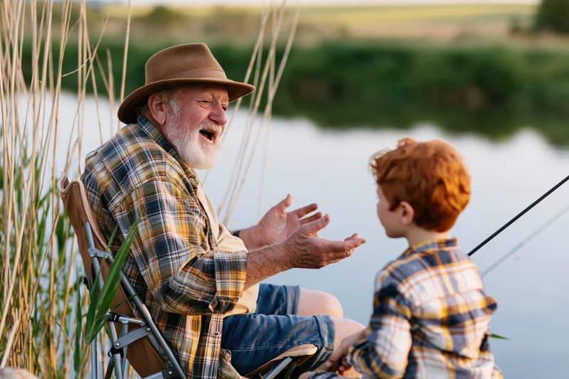 Grandfather telling a story to his grandson by the lake while fishing