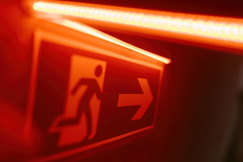 Illuminated emergency exit sign with running figure and arrow on dark wall