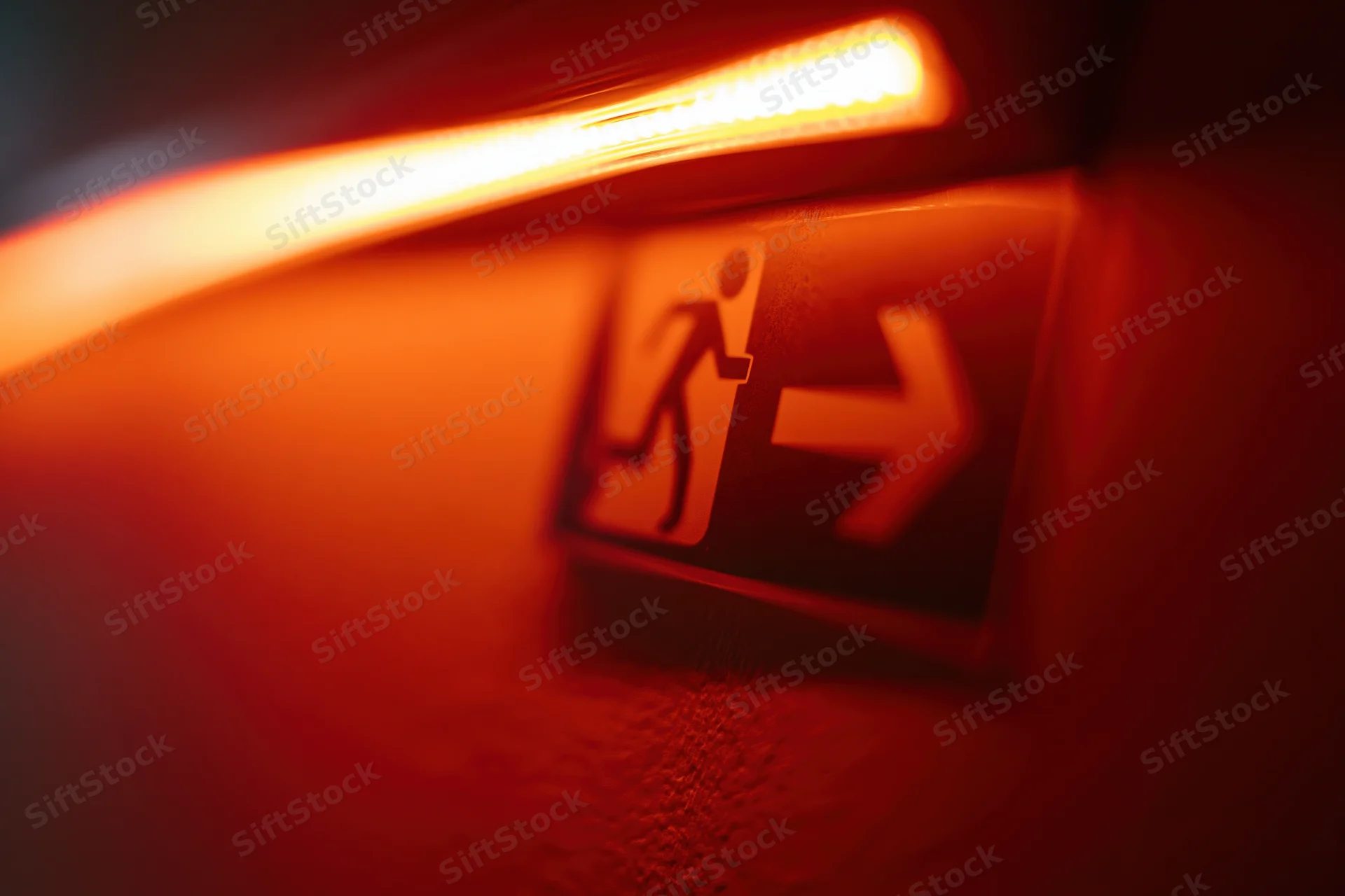 Illuminated emergency exit sign with running figure and arrow on dark wall