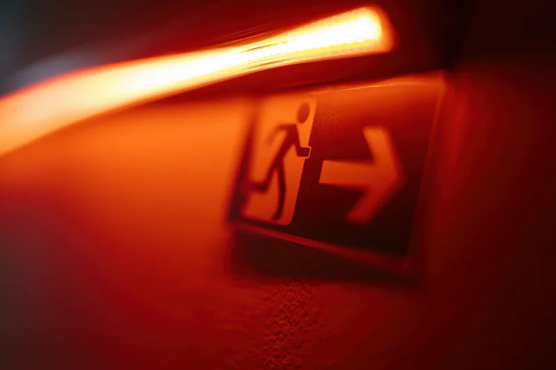 Illuminated emergency exit sign with running figure and arrow on dark wall