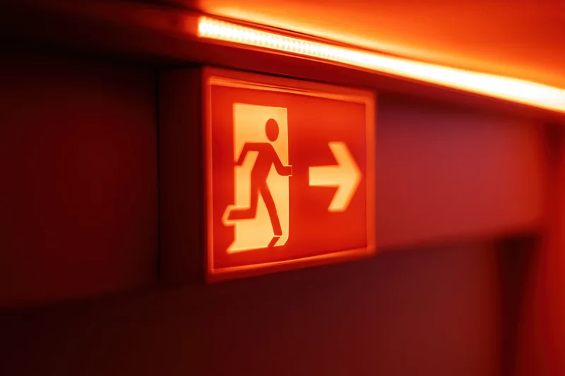 Illuminated emergency exit sign with running figure and arrow mounted on a dark wall in a corridor