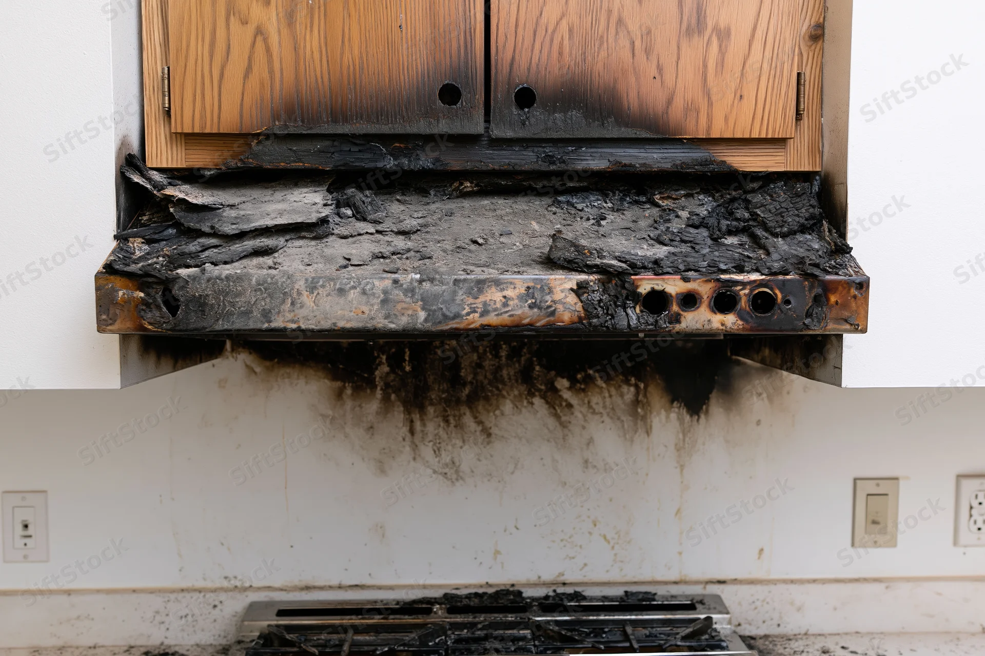 Fire-damaged kitchen range with charred hood and cabinets above stove